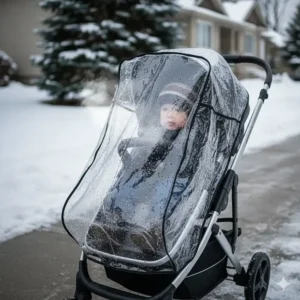A clear, heavy-duty stroller weather shield protecting a child from biting winter winds and freezing rain.
