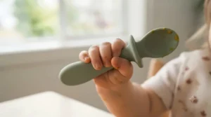 Illustration of an infant hand holding an easy-grip textured spoon, highlighting design features of the best baby utensils for toddlers.